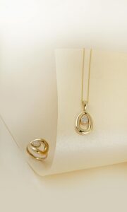Luxurious gold ring and necklace set with diamonds displayed on a soft cream backdrop.